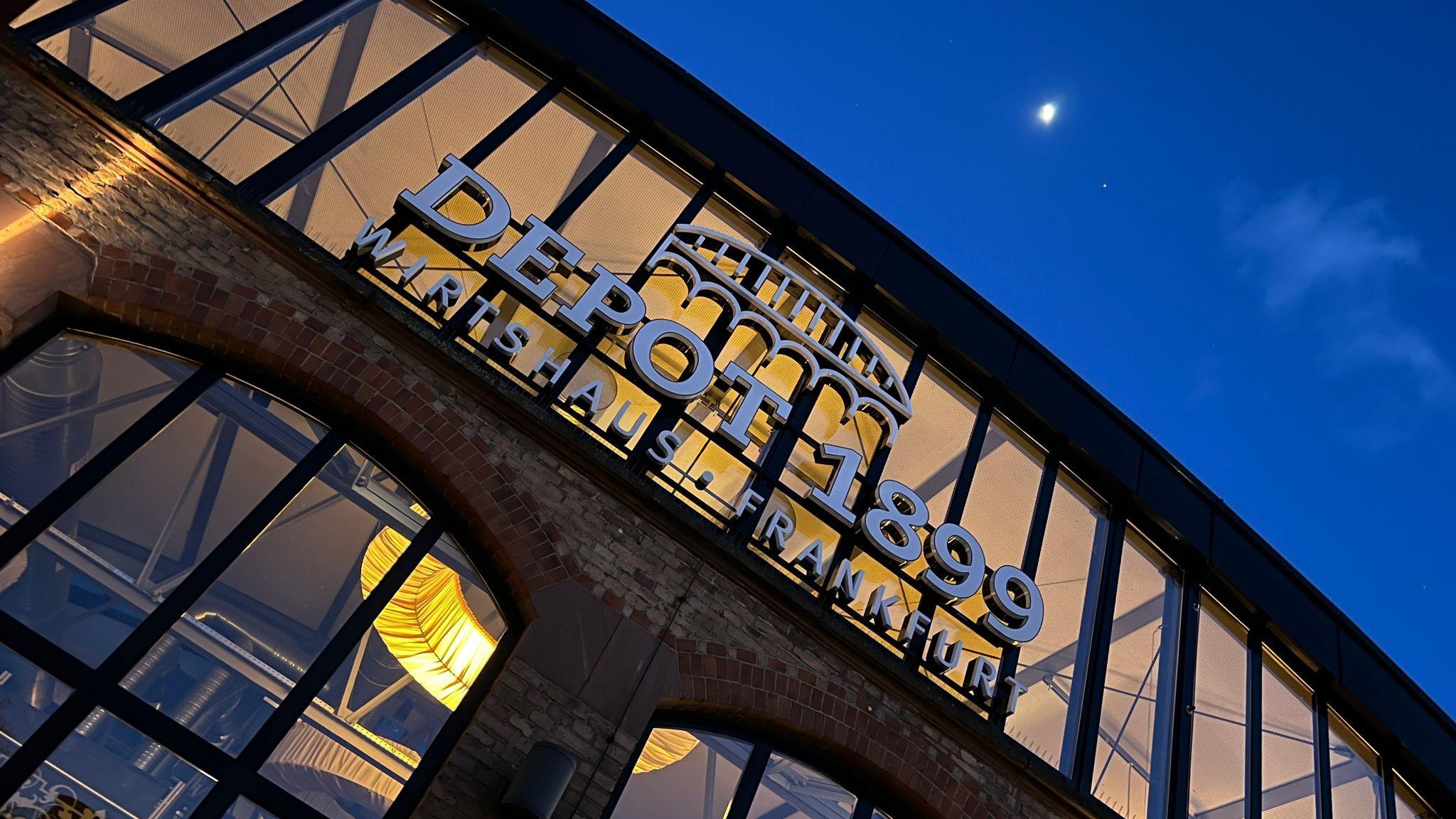 Lit DEPOT 1899 building exterior at night with a visible crescent moon.