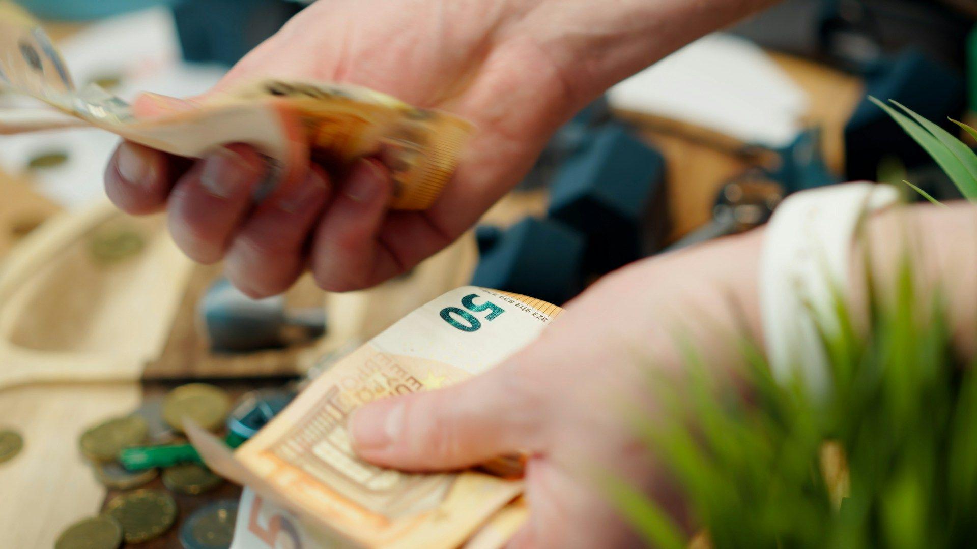 Hands are counting a stack of 50 Euro banknotes on a table with more money.