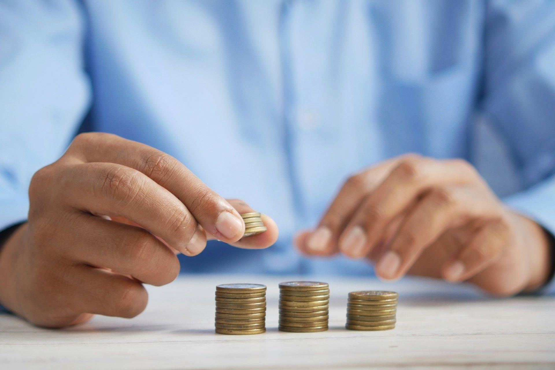 Hands carefully stacking small gold coins into three increasing piles, demonstrating savings.